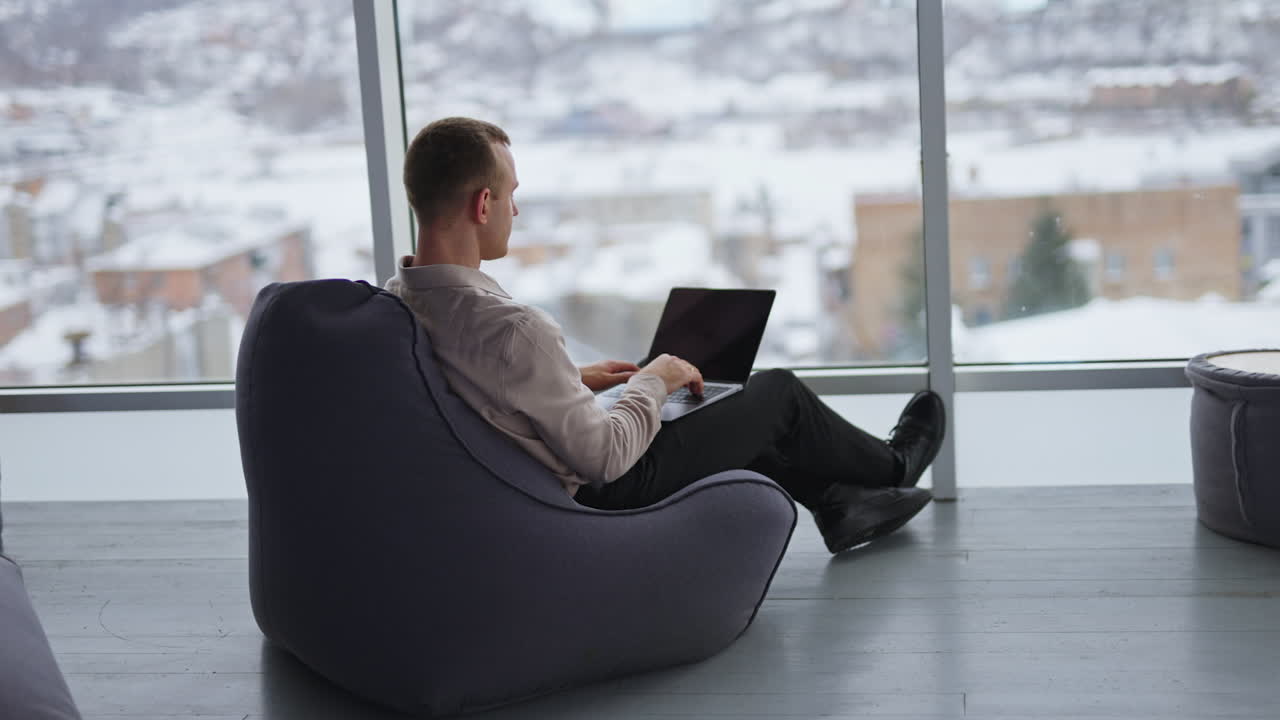 Man working on laptop in a cozy office with a snowy view