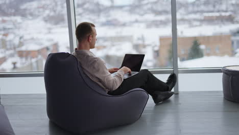 man working on laptop in a cozy office with a snowy view