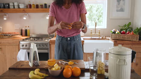 preparing fresh fruit smoothie in kitchen, woman slicing oranges and bananas, at home
