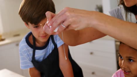madre rompiendo el huevo en el plato mientras los niños la miran en la cocina