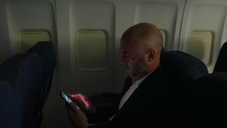 A-man-working-and-browsing-on-a-smartphone-on-a-passenger-airliner-plane-at-night-in-a-dark-cabin