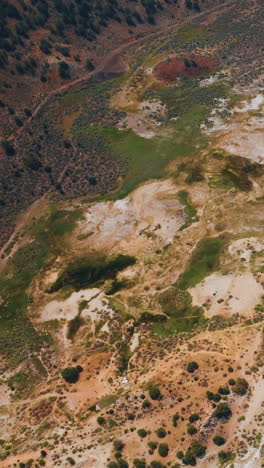 flying over the multi-colored landscape of travertine hot springs in california, usa. rocky scenery with some vegetation growing on. vertical video