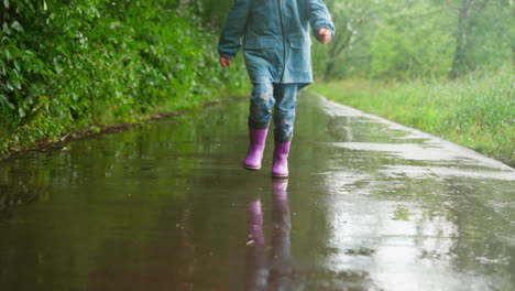 una niña joven con un impermeable y botas de lluvia caminando a través de un charco en la lluvia