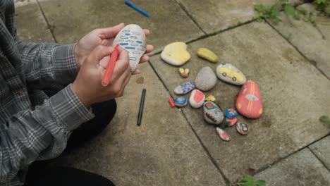 female hands drawing colorful shapes on stones, with markers