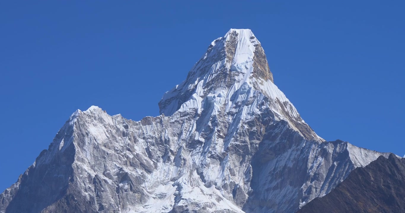 Monte Ama Dablam, una lenta ripresa aerea con drone in avvicinamento verso l'iconica, frastagliata cima innevata dell'Ama Dablam che si innalza in un cielo blu limpido e terso nella regione himalayana del Nepal