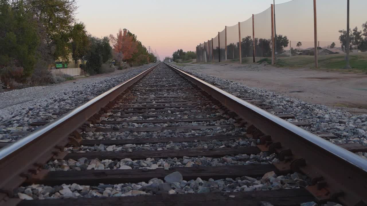 Rising shot over straight empty steel railroad tracks leading to sunset sky