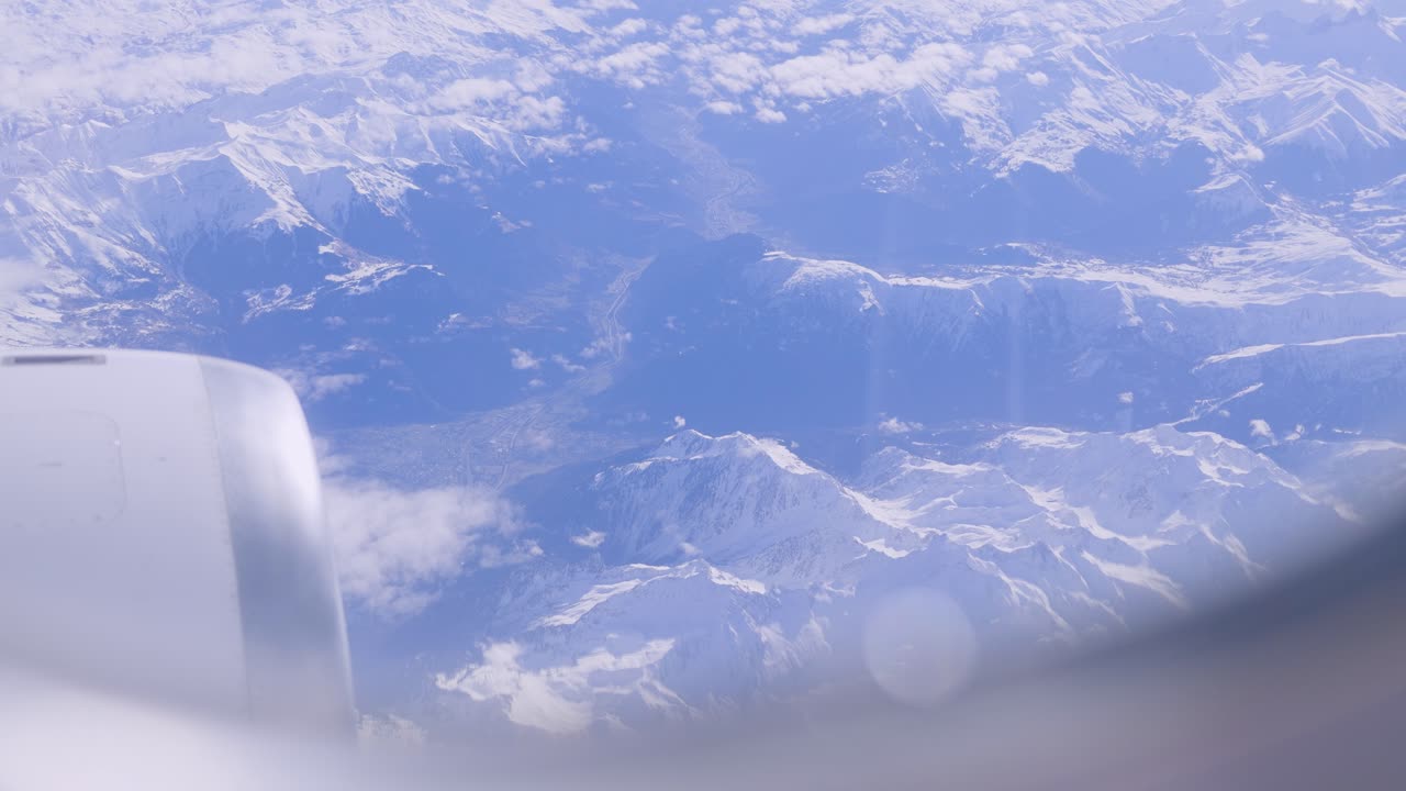 Snow-capped mountains seen from airplane window under a clear sky