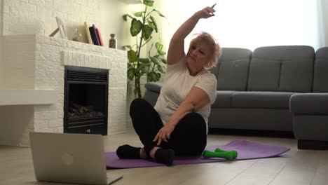 entrenamiento doméstico. mujer mayor activa haciendo ejercicio frente a la computadora portátil en casa, espacio libre