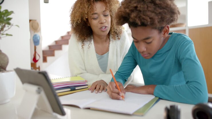 African american mother helping her son with homework using tablet in kitchen, slow motion