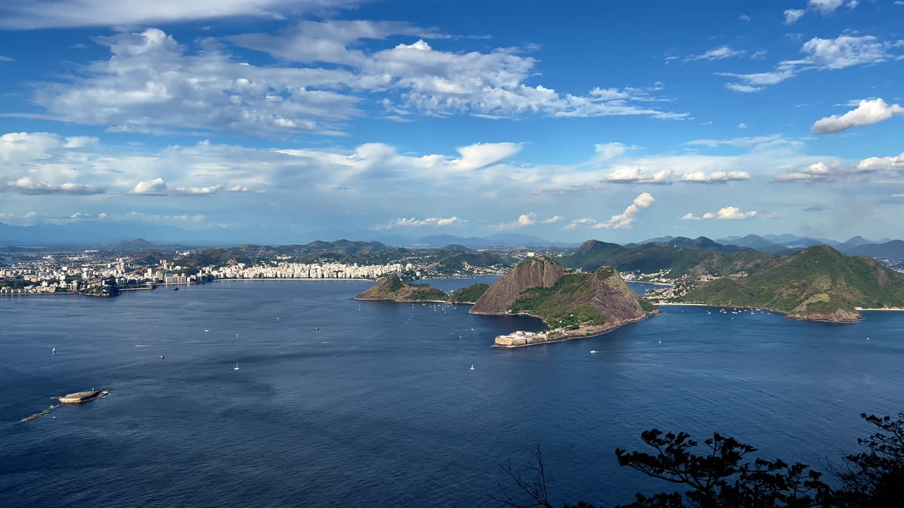 ภาพพาโนรามาจากด้านบนของ Pão de Açúcar ที่มองเห็น Niterói ภาพนี้จับภาพป้อม Santa Cruz อันเก่าแก่ ชายหาด Niterói ที่สวยงาม และผืนน้ำสีฟ้าอันกว้างใหญ่ของอ่าวกัวนาบาราภายใต้ท้องฟ้าเขตร้อนที่ปลอดโปร่ง