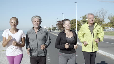 happy active friends jogging on road near sea