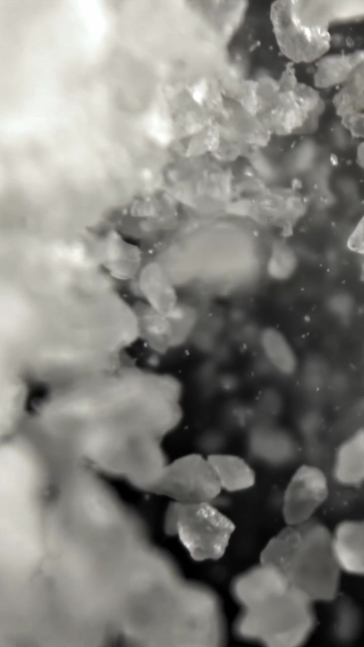 Primo piano macro di cristalli granulari bianchi che cadono su sfondo scuro