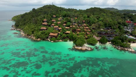 Resort-on-small-tropical-island,-with-blue-water-and-coral-reefs--aerial-rotation