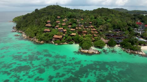 resort en una pequeña isla tropical, con aguas azules y arrecifes de coral- rotación aérea