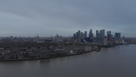 wide falling drone shot of london skyline from canary wharf cloudy