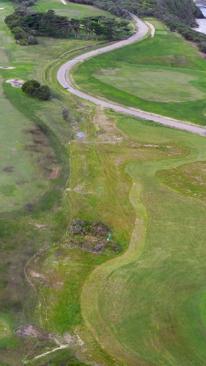 High-angle drone shot of a green golf course and winding road in Flinders, Australia.