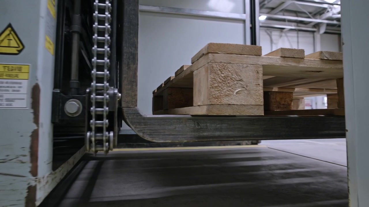 Operatore che aziona i comandi, con le forche del carrello elevatore che trasportano un pallet che entra nella zona di stoccaggio del magazzino