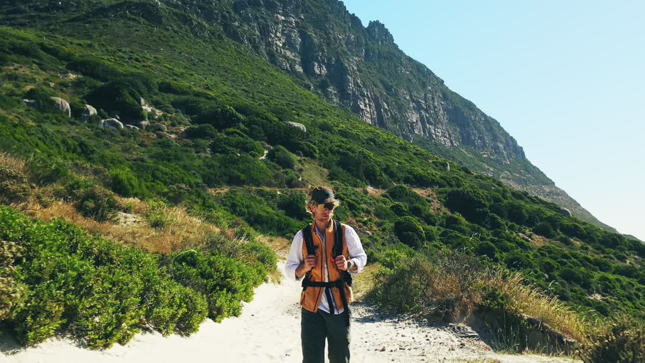 Man Hiking on a Sandy Path with Green Mountains in Background