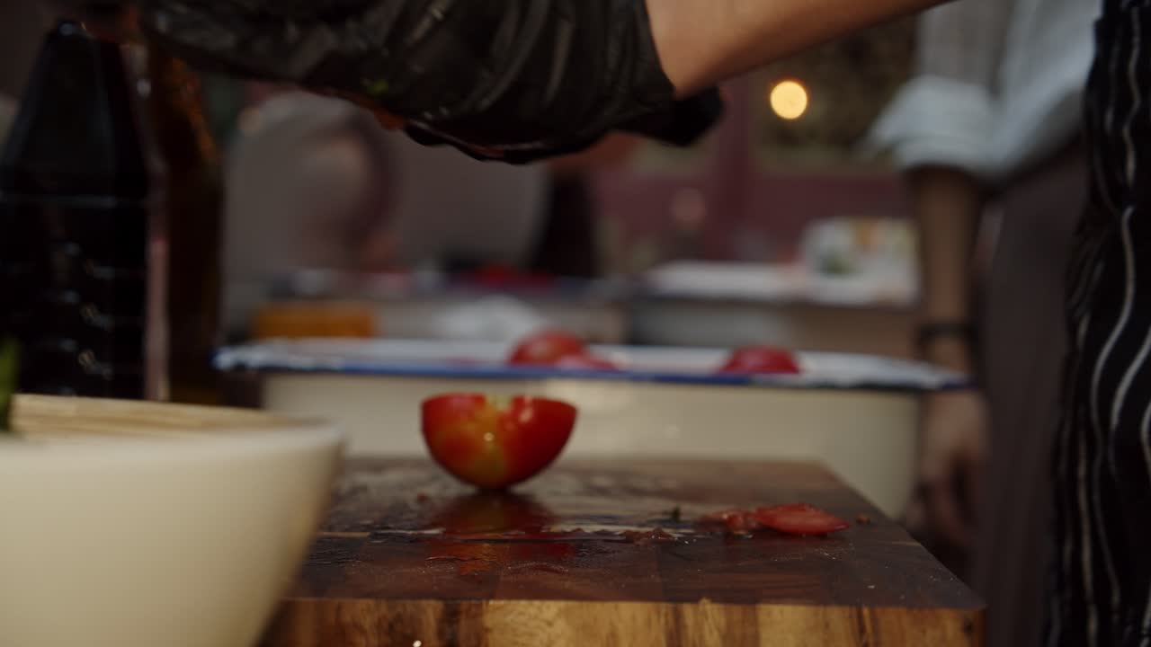 Close up on chef hands in black gloves cutting tomatoes on wooden cut board