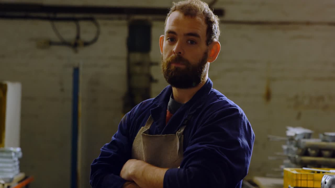 Artigiano del metallo in piedi a braccia conserte in officina 4k