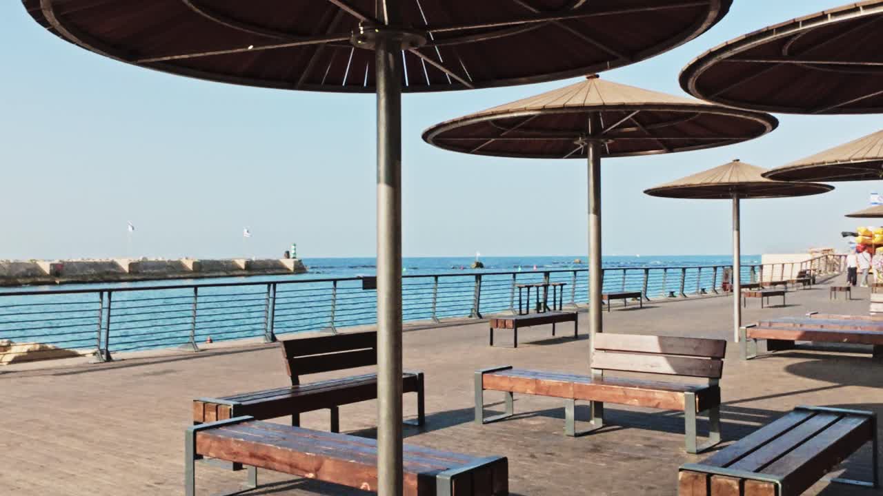 Ombrelloni e panchine in legno sul lungomare del porto di Jaffa, in riva al mare