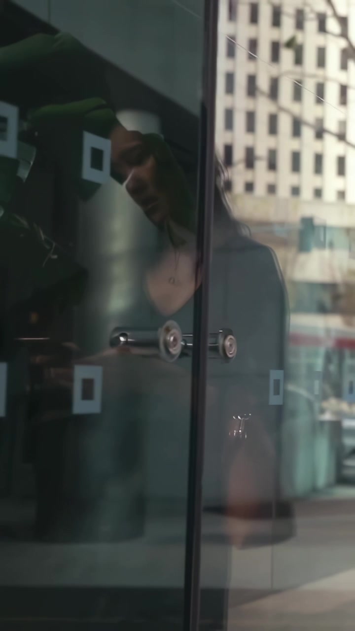 Video vertical: Mujer asiática acercándose a la puerta de cristal de una tienda, usando un teclado para entrar.