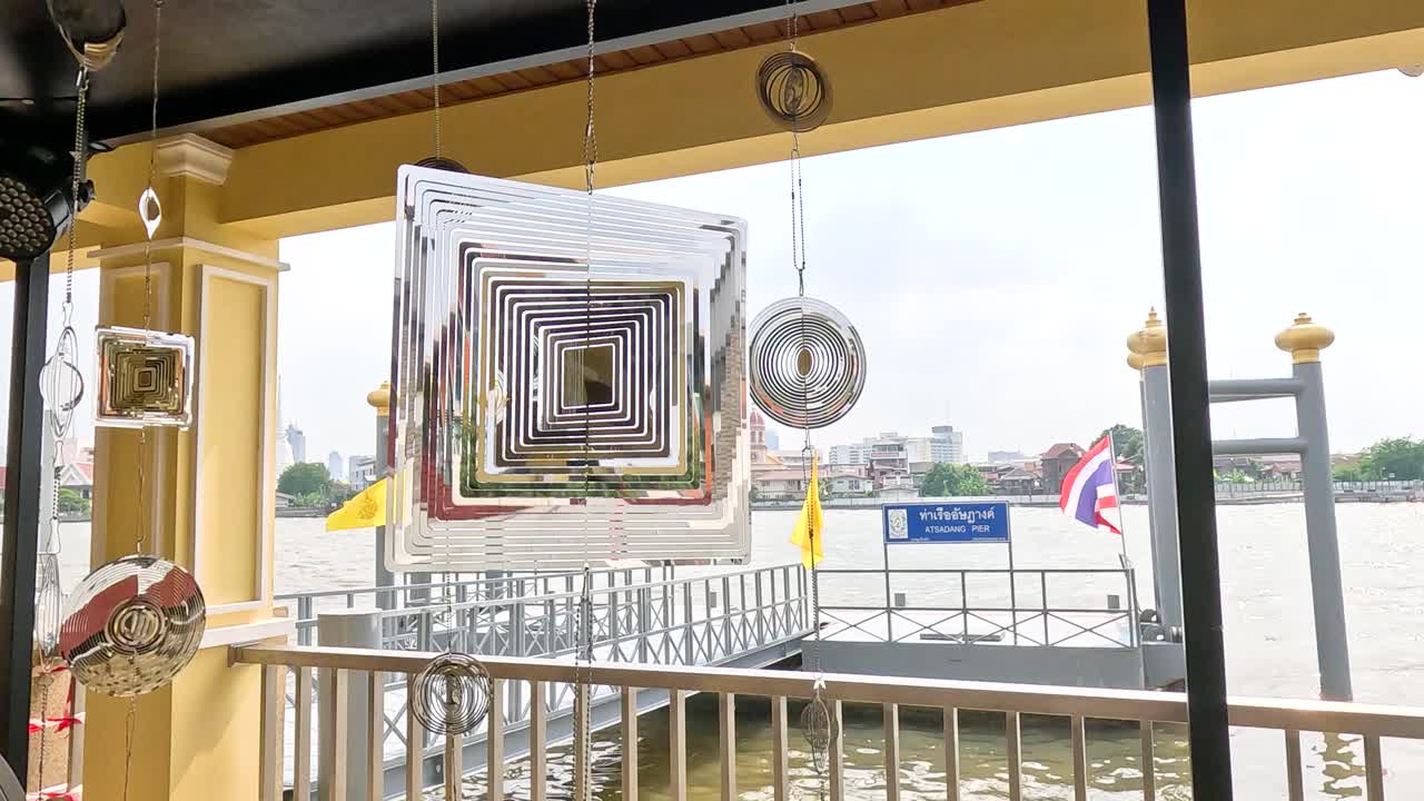 A stainless steel spinner rotates against a riverfront backdrop in Bangkok, Thailand, with bright daylight illuminating the scene