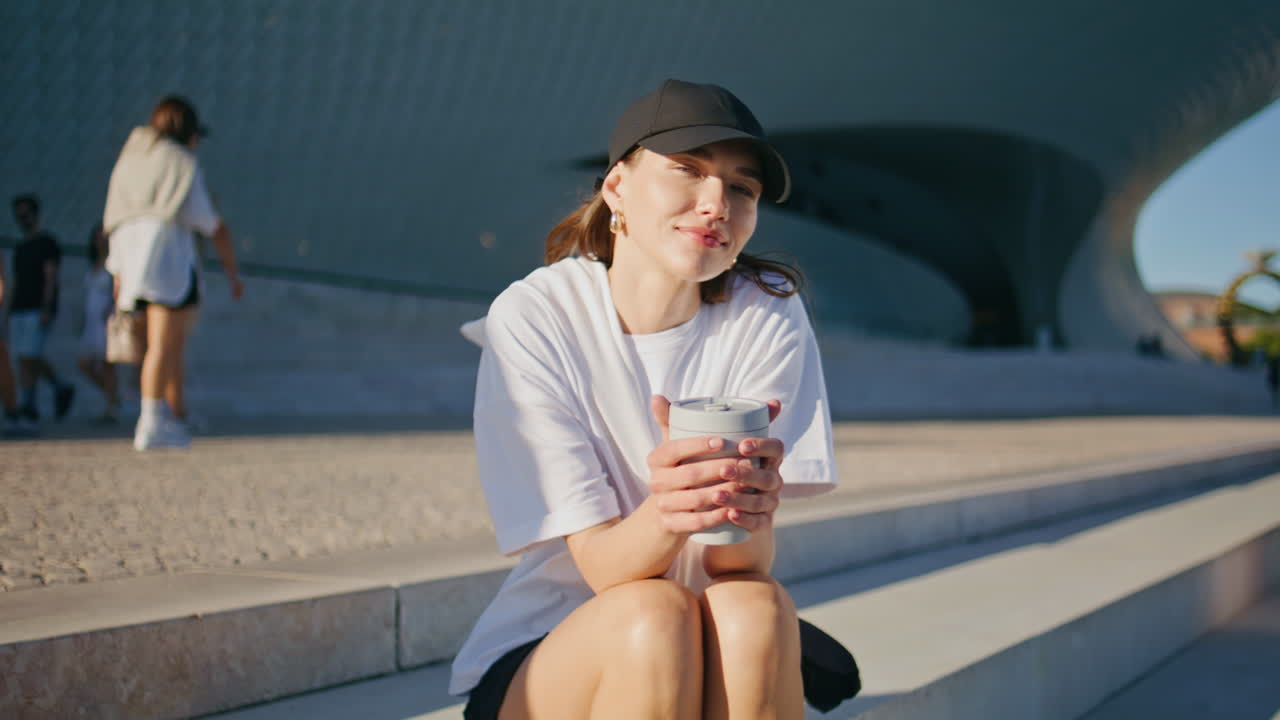 Lady sitting city stairs holding hot beverage cup looking camera with smile