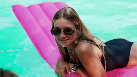 beautiful blonde lady lies wearing black swimsuit and sunglasses lies on the mattress. woman swimming in the pool.