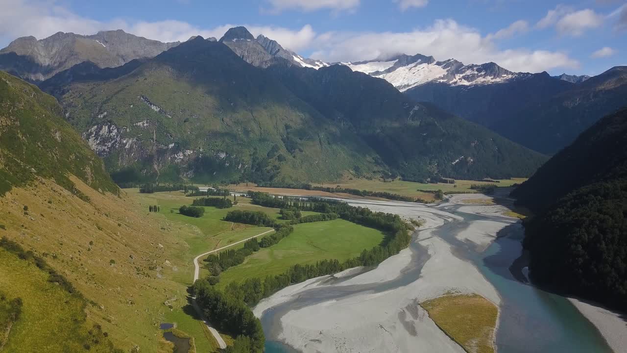 Panoramica verso destra su una vasta valle con un fiume ghiacciato verso una foresta scura sul fianco di una montagna nella regione alpina della Nuova Zelanda