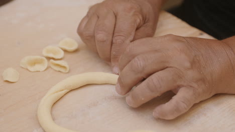 Close-up-footage-of-a-lady-in-Bari,-Italy-cutting-up-a-roll-of-dough-to-make-conchiglie-shells-pasta