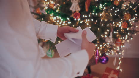 man opening letter with decorated christmas tree in background