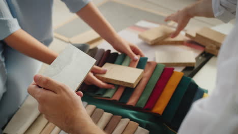 the hands of two designers, sorting and comparing samples of fabric, wood, wallpaper and plaster.