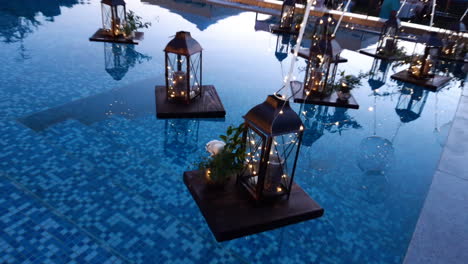 Pool-decor-with-a-romantic-lantern-candle-and-a-vase-of-flowers-float-on-calm-water's-surface