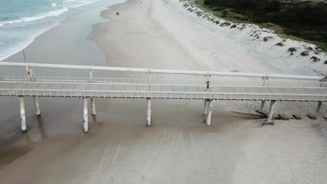 Tiro-De-Drone-De-Mujer-Corriendo-En-El-Muelle-De-La-Playa-En-El-Cuerpo-De-Fitness-De-Verano--gold-Coast-Queensland