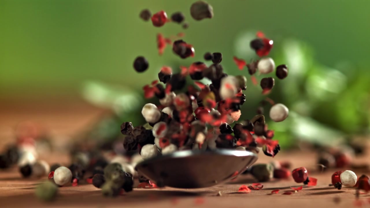 Super slowmotion af blandede peberkorn, der falder fra en ske
