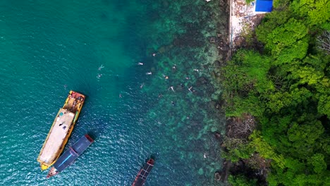 tourist boats surrounding a small tropical island in koh rong, cambodia, with crystal clear water and lush vegetation. amazing aerial view flight vertical bird's eye view drone