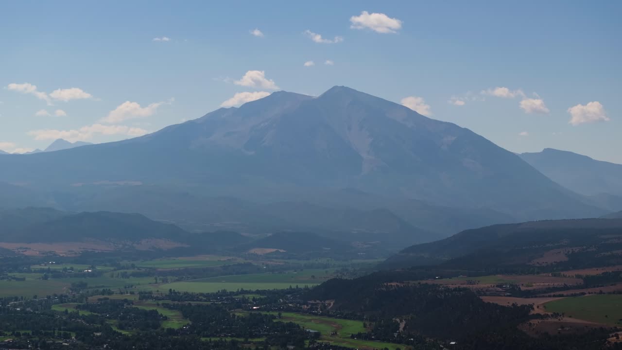 Aerial telephoto ascend establishing Mount Sopris rising above rolling foothills under clear late day Colorado light