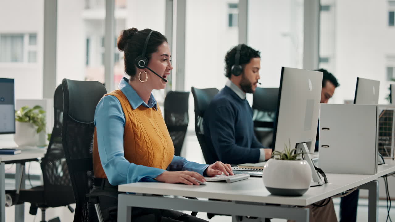 Smilende kvinne med hodesett jobber på datamaskin i et moderne kontor