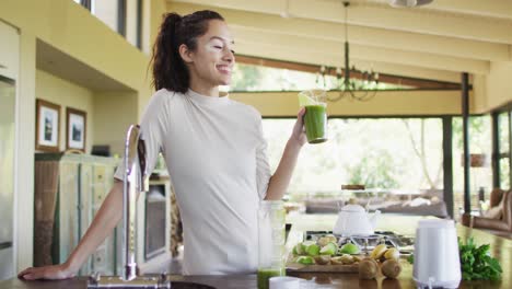 happy biracial woman drinking smoothie in kitchen