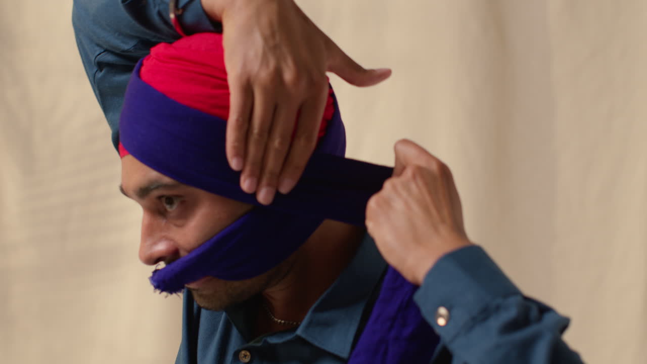 fotografía de estudio de cerca de un hombre sikh atando tela para un turbante contra un fondo plano