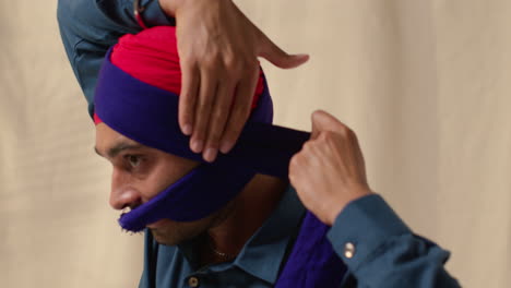 close up studio shot di un uomo sikh che lega tessuto per un turbante contro uno sfondo semplice