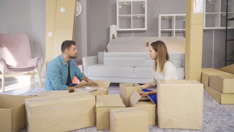 Smiling-young-couple-move-into-a-new-home-sitting-on-floor-and-unpacking.