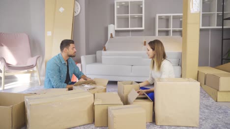 una joven pareja sonriente se muda a una nueva casa sentada en el suelo y desempaquetando.
