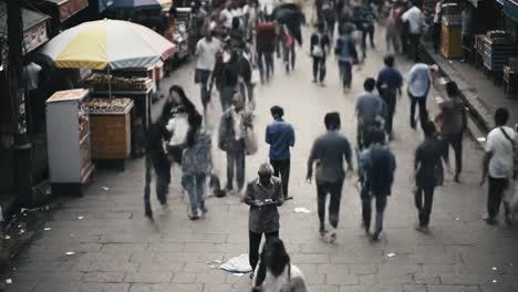 a lively market filled with people moving about. in the center, a solitary individual stands still, engrossed in their phone amid the activity surrounding them.