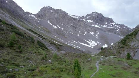 aerial drone footage flying slowly through a glacial mountain landscape with patches of snow, isolated trees a remote alpine hiking trail in switzerland