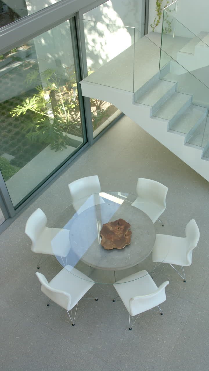 Vertical video: Modern dining area with glass table and white chairs in bright home