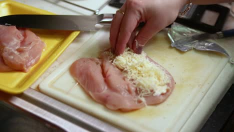 agregando queso rallado encima de la pechuga de pollo cruda precortada