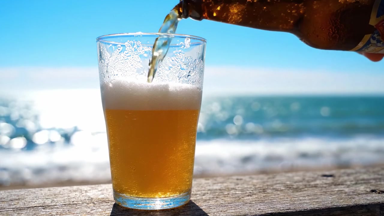 Birra rinfrescante versata in un bicchiere su una spiaggia panoramica, catturando l'essenza della felicità estiva e del relax in una splendida cornice costiera.