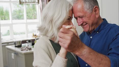 pareja caucásica romántica en casa bailando en la cocina y sonriendo
